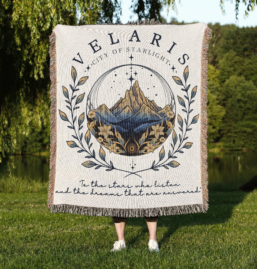Person holding a blanket with 'Velaris City of Starlight' design outdoors.