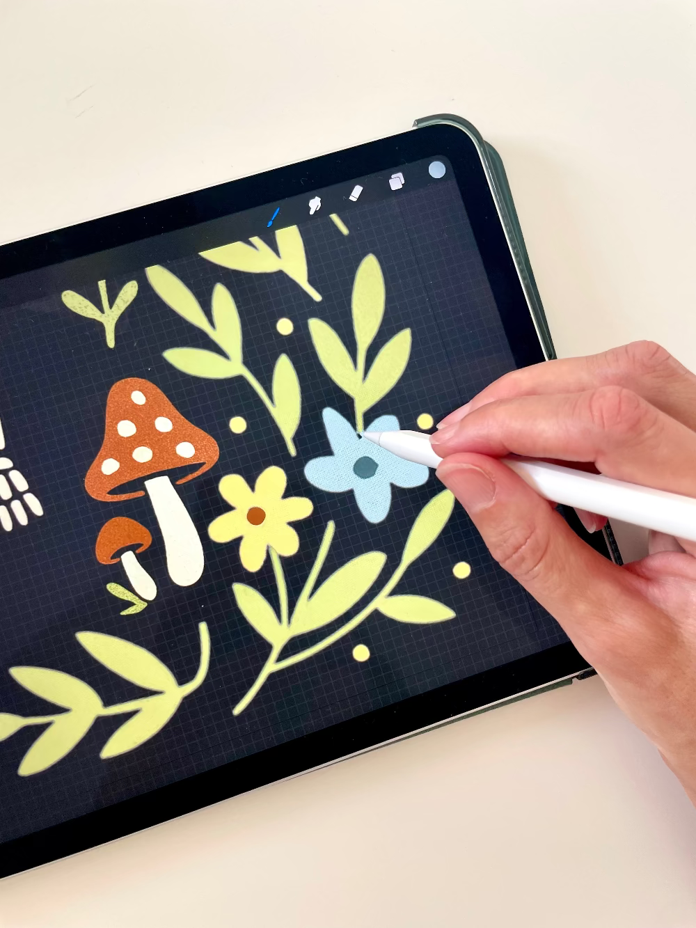 Person using a stylus to draw on a digital tablet with floral and mushroom designs.