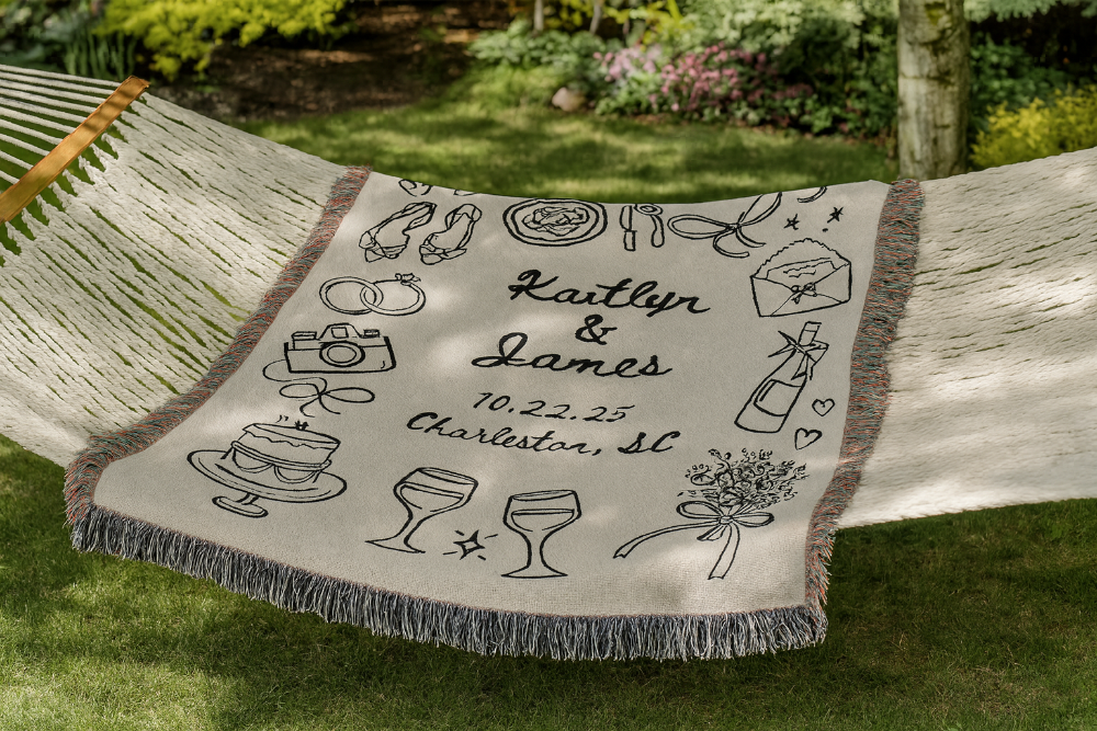Personalized blanket with wedding details hanging on a wooden bench outdoors.